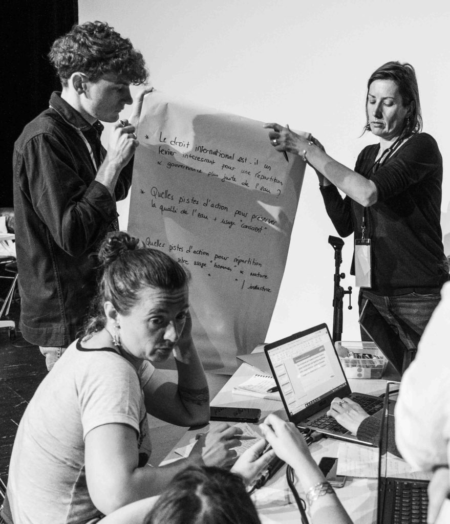Deux personnes tenant une feuille de paper board sur lequel il est écrit : « le droit international est-il un levier intéressant pour une répartition et gouvernance plus juste de l'eau ? »