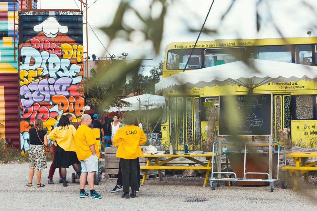 Bus jaune, personnes habillées en jaune, avec une chemise estampillée "Labo" allant à la rencontre d'habitants.