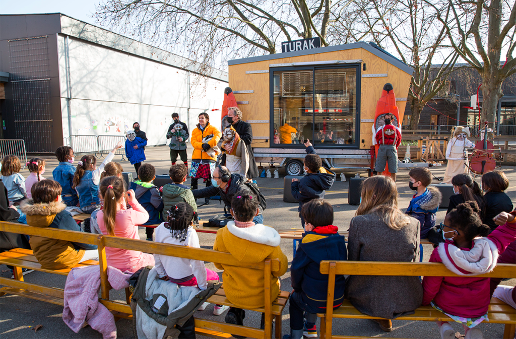 Dans leur cour de récréation, de jeunes élèves assistent à un spectacle. Sur scène, on aperçoit une caravane où il est inscrit "Turak", le nom de la résidence de théâtre.