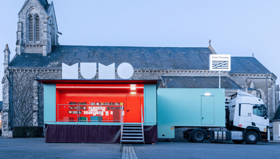 Le camion MuMo se trouve sur une place devant l'église d'un village. Il est ouvert : on aperçoit à l'intérieur des papiers affichés sur les murs. On devine alors une salle d'exposition. 